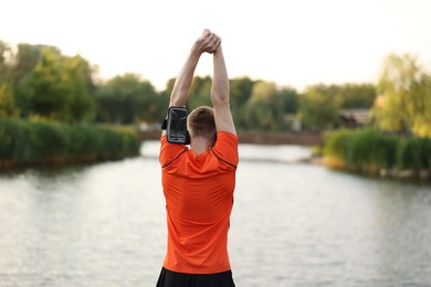 Photo of Sportsman in armband doing morning exercise near river, back view