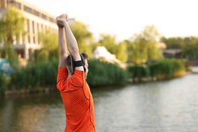 Photo of Sportsman in headphones and armband doing morning exercise near river. Space for text