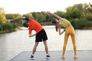Photo of Couple in headphones doing morning exercise on pier near river, back view