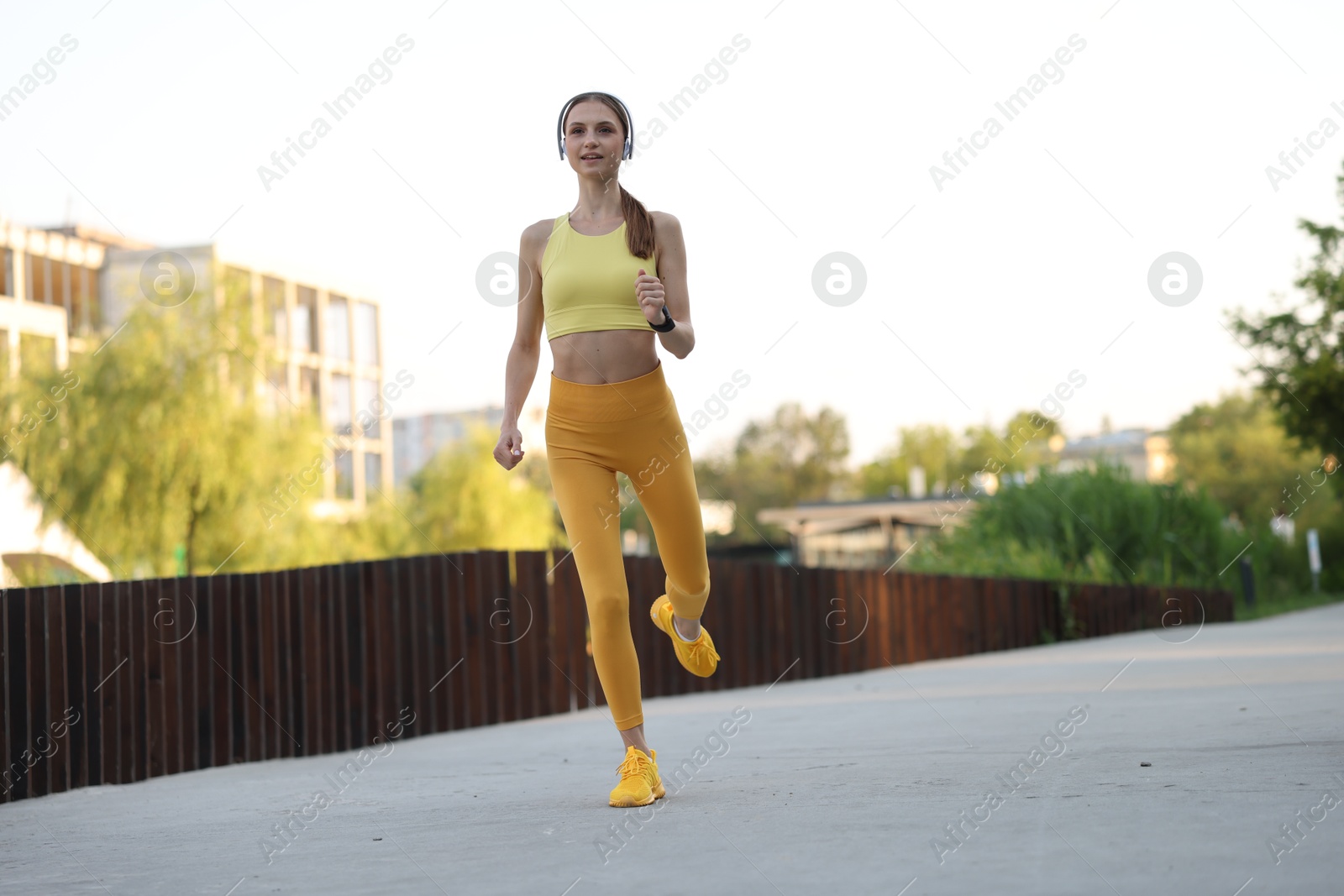 Happy sportswoman in headphones running outdoors, low angle view. Morning exercise Photo of Happy sportswoman in headphones running outdoors, low angle view. Morning exercise