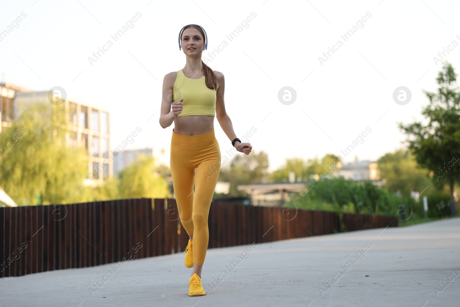 Happy sportswoman in headphones running outdoors, low angle view. Morning exercise Photo of Happy sportswoman in headphones running outdoors, low angle view. Morning exercise