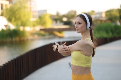 Photo of Young sportswoman in headphones doing morning exercise outdoors. Space for text