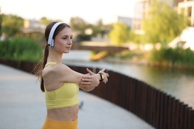 Photo of Young sportswoman in headphones doing morning exercise outdoors. Space for text