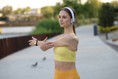 Photo of Young sportswoman in headphones doing morning exercise outdoors