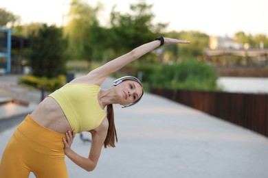 Photo of Young sportswoman in headphones doing morning exercise outdoors