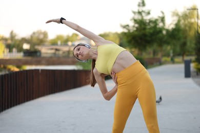 Photo of Young sportswoman in headphones doing morning exercise outdoors