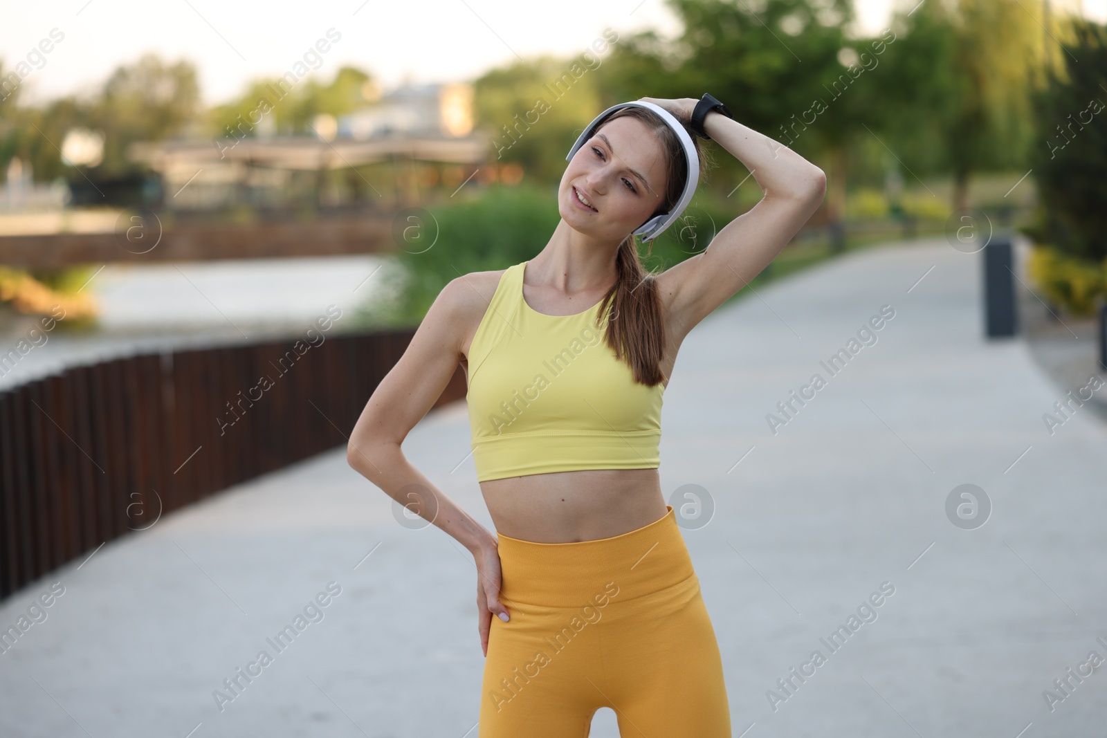 Smiling sportswoman in headphones doing morning exercise outdoors Photo of Smiling sportswoman in headphones doing morning exercise outdoors