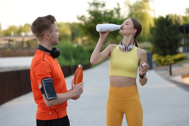 Photo of Happy couple drinking water after morning exercises outdoors