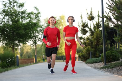 Photo of Happy couple in headphones running outdoors, low angle view. Morning exercise