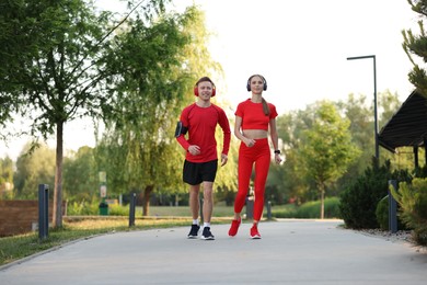 Photo of Happy couple in headphones running outdoors, low angle view. Morning exercise