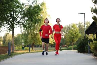 Photo of Happy couple in headphones running outdoors, low angle view. Morning exercise