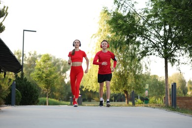 Photo of Happy couple in headphones running outdoors, low angle view. Morning exercise