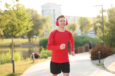 Photo of Smiling sportsman in headphones running outdoors. Morning exercise