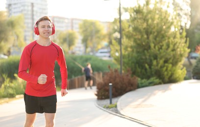 Photo of Smiling sportsman in headphones running outdoors, space for text. Morning exercise