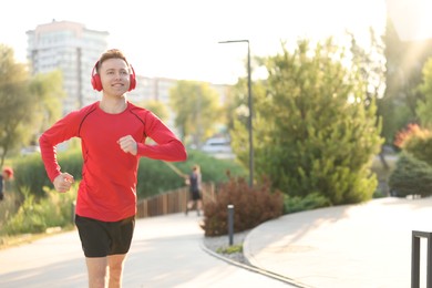 Photo of Smiling sportsman in headphones running outdoors, space for text. Morning exercise