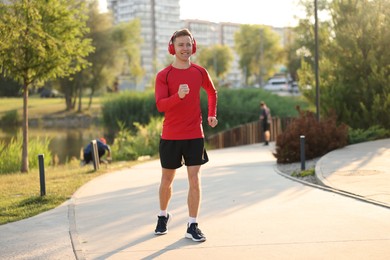 Photo of Smiling sportsman in headphones running outdoors. Morning exercise