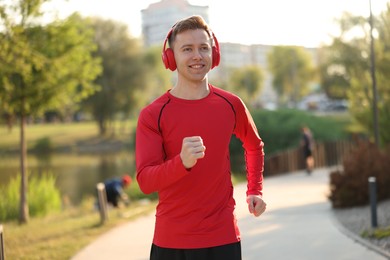 Photo of Smiling sportsman in headphones running outdoors. Morning exercise