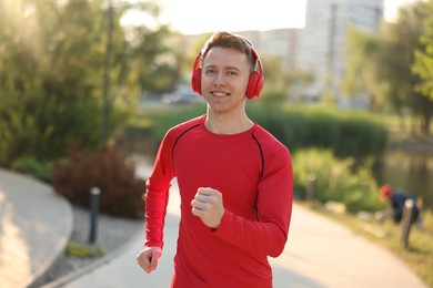 Photo of Smiling sportsman in headphones running outdoors. Morning exercise
