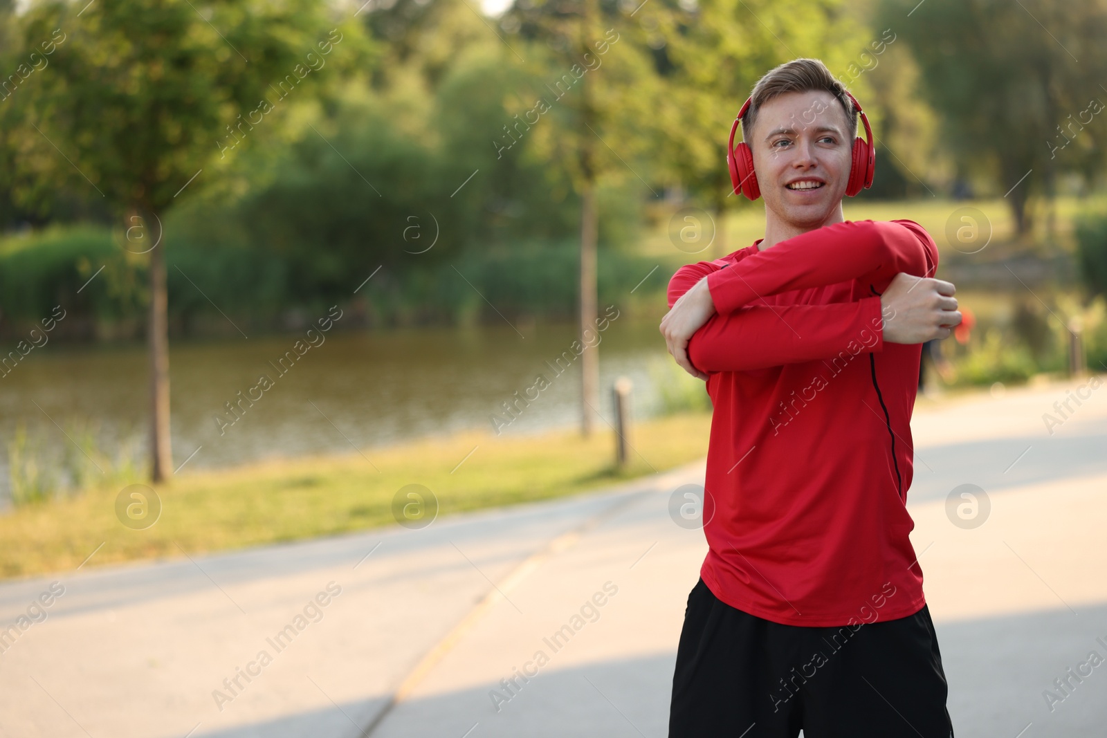 Smiling sportsman in headphones doing morning exercise outdoors. Space for text Photo of Smiling sportsman in headphones doing morning exercise outdoors. Space for text