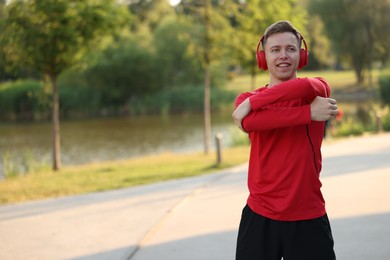 Photo of Smiling sportsman in headphones doing morning exercise outdoors. Space for text