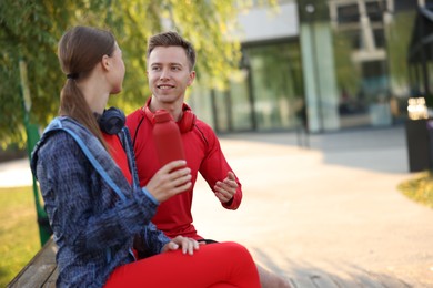 Photo of Happy couple resting on bench after morning exercises outdoors. Space for text