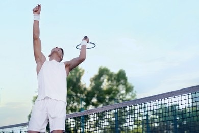 Photo of Young man playing tennis at court on sunny day, low angle view. Space for text