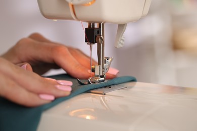 Photo of Woman working with sewing machine and fabric in workshop, closeup