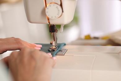 Photo of Woman working with sewing machine and fabric in workshop, closeup