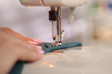 Photo of Woman working with sewing machine and fabric in workshop, closeup