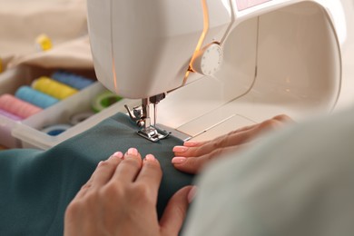 Photo of Woman working with sewing machine and fabric in workshop, closeup