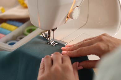 Photo of Woman working with sewing machine and fabric in workshop, closeup