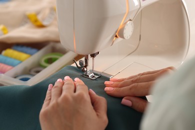 Photo of Woman working with sewing machine and fabric in workshop, closeup