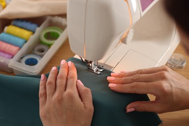 Photo of Woman working with sewing machine and fabric at table in workshop, closeup