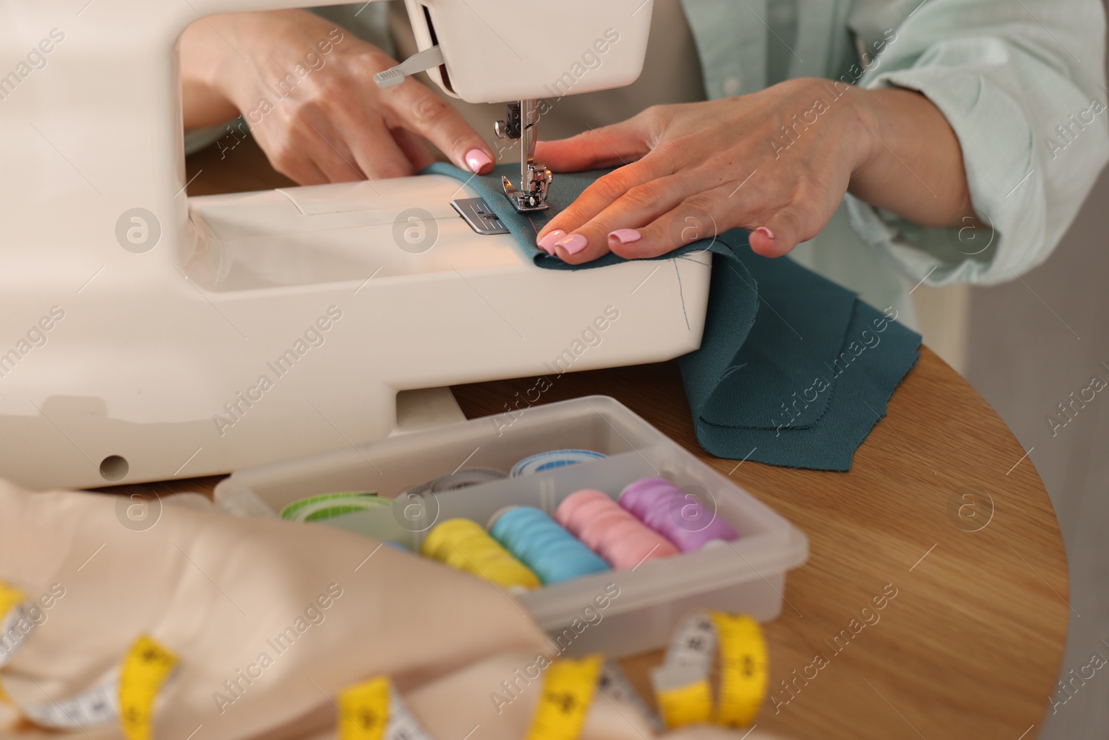 Woman working with sewing machine and fabric at table in workshop, closeup Photo of Woman working with sewing machine and fabric at table in workshop, closeup