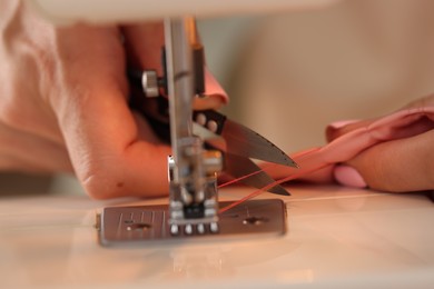 Photo of Woman working with sewing machine and fabric in workshop, closeup