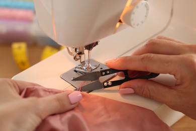 Photo of Woman working with sewing machine and fabric in workshop, closeup