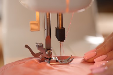 Photo of Woman working with sewing machine and fabric in workshop, closeup
