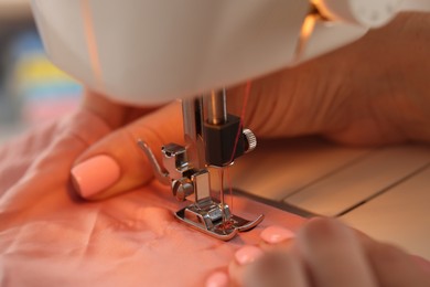 Photo of Woman working with sewing machine and fabric in workshop, closeup