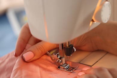 Photo of Woman working with sewing machine and fabric in workshop, closeup
