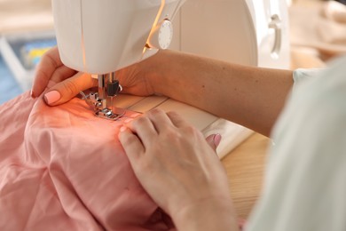 Photo of Woman working with sewing machine and fabric in workshop, closeup