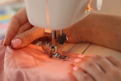 Photo of Woman working with sewing machine and fabric in workshop, closeup