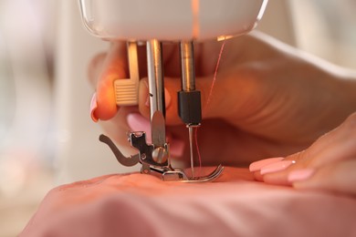 Photo of Woman working with sewing machine and fabric in workshop, closeup
