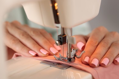 Photo of Woman working with sewing machine and fabric in workshop, closeup