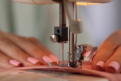 Photo of Woman working with sewing machine and fabric in workshop, closeup