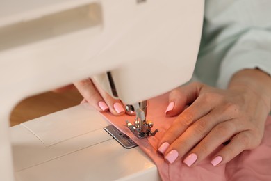 Photo of Woman working with sewing machine and fabric in workshop, closeup