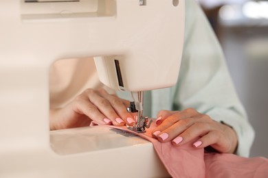 Photo of Woman working with sewing machine and fabric in workshop, closeup