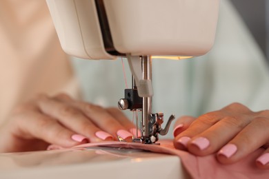 Photo of Woman working with sewing machine and fabric in workshop, closeup