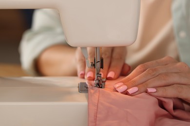 Photo of Woman working with sewing machine and fabric in workshop, closeup