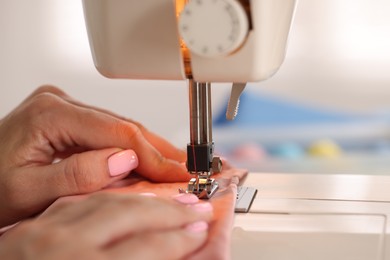 Photo of Woman working with sewing machine and fabric in workshop, closeup