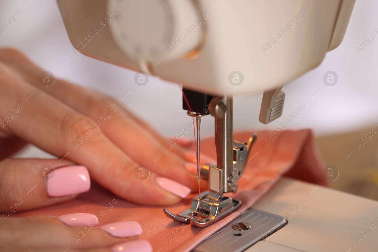 Photo of Woman working with sewing machine and fabric in workshop, closeup